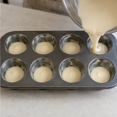 Step 3: Divide the batter evenly among the 8 greased cavities, filling each about two-thirds full. Tap the tin gently on the counter to release large air bubbles. Do not overfill, as the cakes rise while baking.