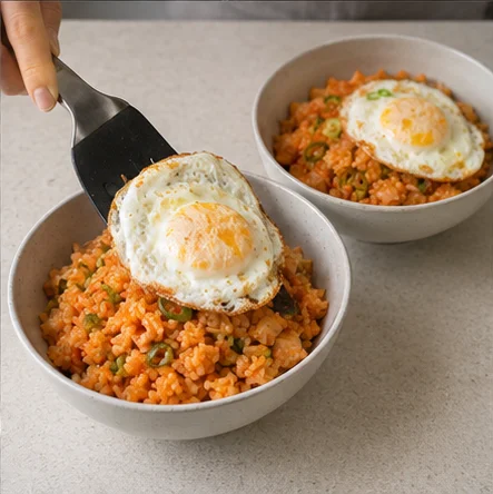Paso 6: Reparte el arroz caliente en dos boles y añade un huevo a cada uno. Sirve enseguida. Prueba antes de añadir sal: el kimchi ya es salado y su sabor cambia según la marca.