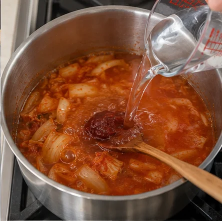 Étape 3: Ajoutez 600 ml d’eau, 1 c. à soupe de gochujang et 1 c. à café de sauce soja. Décollez doucement les sucs du fond et dissolvez la pâte dans le bouillon.