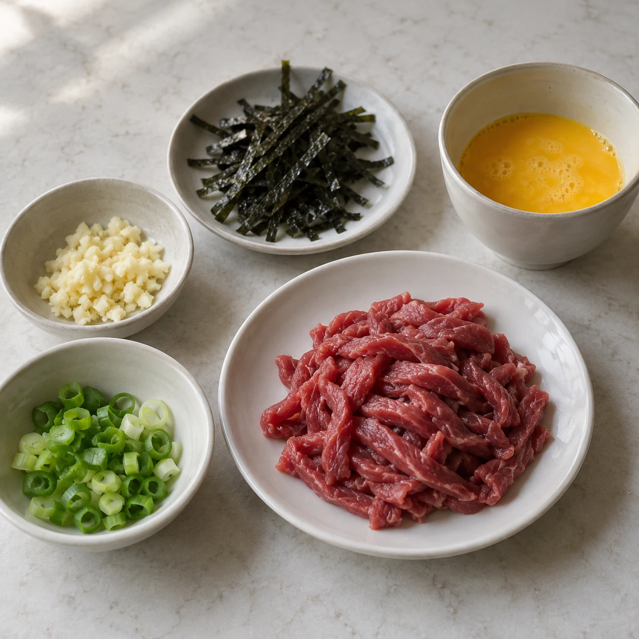 ขั้นตอน 2: หั่นเนื้อวัวเป็นเส้นเล็กๆ บางๆ สับต้นหอม สับกระเทียม ตีไข่ในถ้วย แล้วตัดโนริเป็นเส้นสั้น แยกเนื้อดิบออกจากเครื่องปรุง